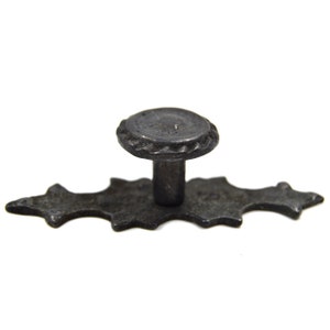 Może przedstawiać: Czarna metalowa gałka do szafki z wzorem gwiazdy i okrągłym pokrętłem. Gałka jest przymocowana do metalowej płytki z wzorem gwiazdy.