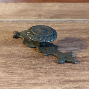 May include: A black metal cabinet knob with a decorative, ornate design. The knob has a round, fluted top and a long, pointed base.