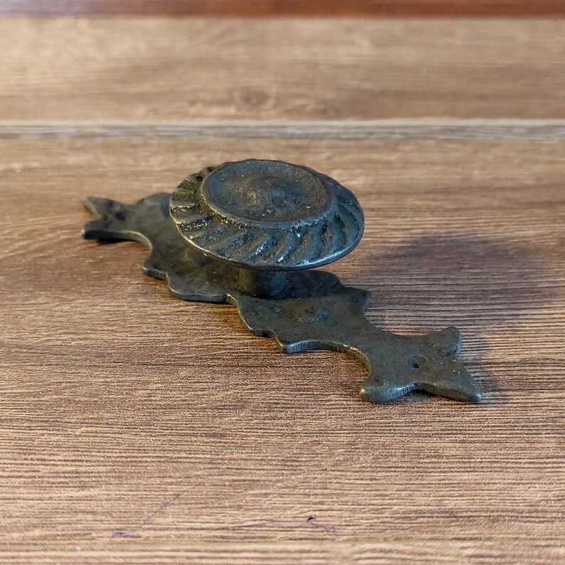 May include: A black metal cabinet knob with a decorative, ornate design. The knob has a round, fluted top and a long, pointed base.