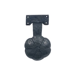 Op de afbeelding: Zwarte metalen deurknop met een bloemvormig ontwerp. De knop heeft een rechthoekige basis met twee schroeven en een T-vormige steel.