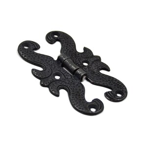 May include: Black metal hinge with a decorative, ornate design. The hinge is made of two pieces that are connected by a metal pin.