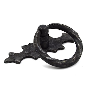 Op de afbeelding: Zwarte metalen ringtrekhengsel met een decoratieve, sierlijke basis. De hendel is ontworpen voor kasten, lades of deuren.