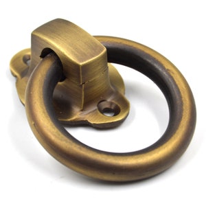 以下が含まれることがあります： 正方形のベースと丸いリングが付いた真鍮製のリングプルハンドル。ハンドルは使い古した仕上げで、アンティークな外観になっています。