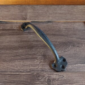 May include: A black metal door handle with a star-shaped design. The handle is on a wooden surface.