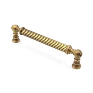May include: A gold-toned cabinet pull with a fluted design and rounded ends. The pull is approximately 6 inches long.