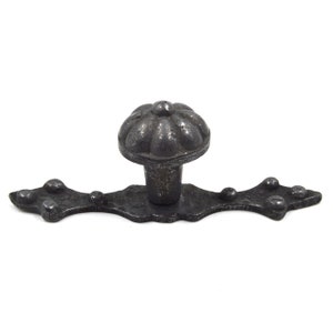 Könnte beinhalten: Schwarzer Metall-Schrankknauf mit einem dekorativen, geriffelten, runden Kopf und einer langen, flachen Basis mit einem gewellten Rand und dekorativen Nieten.