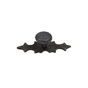 Może przedstawiać: Czarny metalowy gałka do szafki z ozdobną, falistą podstawą i okrągłym, fakturowanym gałką.