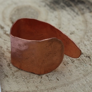 Può includere: Un anello in rame con finitura martellata. L'anello è aperto e ha una forma leggermente curva.