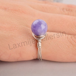 Peut inclure: Une bague artisanale ornée d'une pierre précieuse ronde de couleur lavande. La pierre est maintenue par un fil d'argent délicat. Un bijou unique.