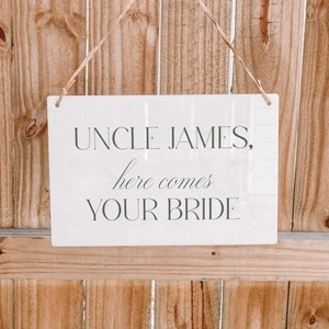 May include: White sign with the text "Uncle James, here comes your bride" hanging from a string.