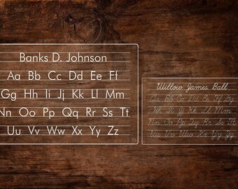 May include: Two white framed dry erase boards with black lines for writing. The top board has the name "Banks D. Johnson" written on it and the alphabet written in cursive. The bottom board has the name "Willow James Ball" written on it and the alphabet written in cursive.