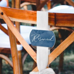 May include: A wooden chair with a white ribbon and a round, blue sign that says "Reserved" in white cursive.