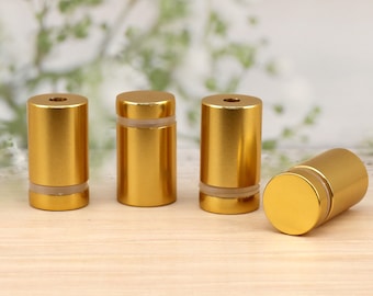 May include: Four gold-colored metal standoffs with a clear plastic insert. The standoffs are arranged in a row on a light wood surface.