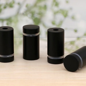 May include: Four black cylindrical bottle stoppers with a silver band around the middle.