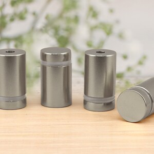 May include: Four silver metal standoffs with clear plastic inserts. The standoffs are cylindrical in shape and have a smooth, polished finish.