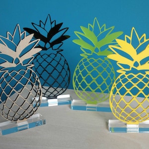 Può includere: Quattro sculture decorative a forma di ananas su basi in acrilico trasparente. Gli ananas sono in legno e sono dipinti in nero, beige, verde e giallo.