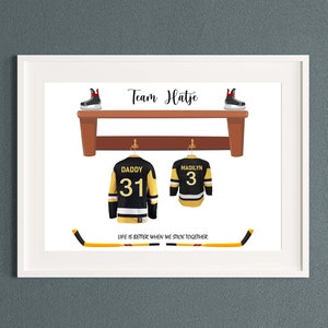 Op de afbeelding: Een wit ingelijst print met de tekst "Team Hatje" en een hockeystick met de tekst "Het leven is beter als we samen scoren". Twee hockeytruien hangen aan haken boven een houten plank met twee paar schaatsen op de plank. De truien zijn zwart met gele en witte accenten. E&eacute;n trui heeft nummer 31 en de tekst "Daddy" op de rug. De andere trui heeft nummer 3 en de tekst "Maclyn" op de rug.