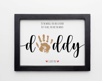 May include: A framed print with a handprint in the centre of the word "daddy". The print reads "To the world, you are a father, but to me, you are the world." and "I love you" with two red hearts.