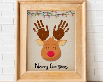 May include: A framed print with a handprint reindeer design. The reindeer has a red nose and the text "Merry Christmas" is printed below the reindeer.