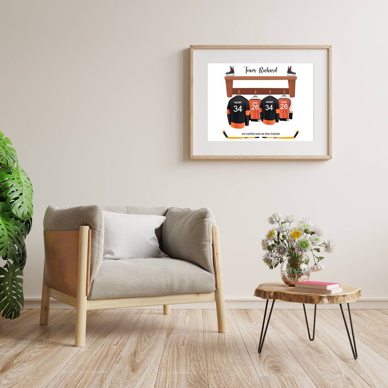 Op de afbeelding: Een ingelijst print met een hockeythema. Het toont een houten plank met drie hockeytruien die aan haken hangen. De truien zijn zwart met oranje accenten en hebben de nummers 34 en 26. De tekst "Team Richard" staat bovenaan de print. De tekst "Life is better when we cheer together" staat onderaan de print.