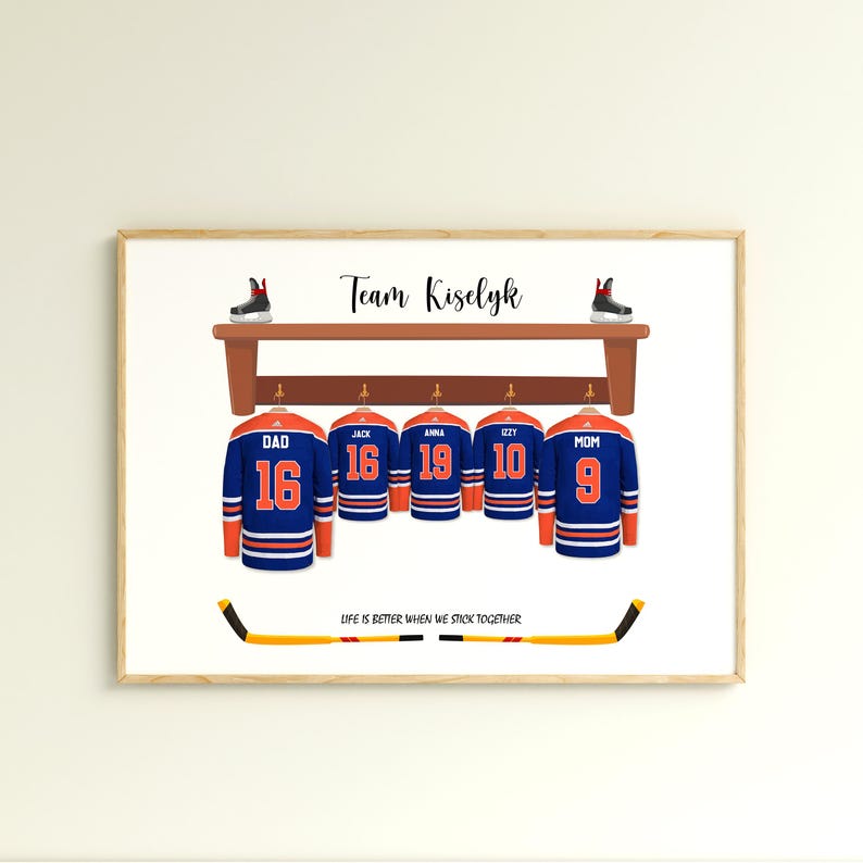 May include: A framed print featuring hockey jerseys with names and numbers, hanging on a wooden rack. The jerseys are blue and orange, with the text "Team Kiselyk" above. A hockey stick and skates are also included.