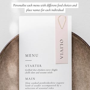 May include: A white menu card with a pink place card attached to it with a gold wire. The place card says "OLIVIA". The menu card says "MENU" and lists a starter and main course.