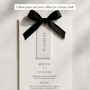 May include: A white menu card with the name "JESSICA" on a tag, tied with a black satin ribbon. The menu includes "STARTER" and "MAIN" course options. Text at the top reads "Vellum paper and satin ribbon for a luxury look!"