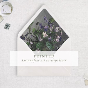 May include: A white envelope with a pointed flap featuring an interior liner printed with a botanical illustration of purple and white violets and green leaves against a dark gray background. The text PRINTED Luxury fine art envelope liner is visible.