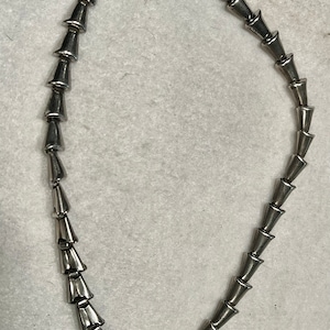 May include: A silver necklace with a chain made of connected cone-shaped links. The necklace has a clasp closure.