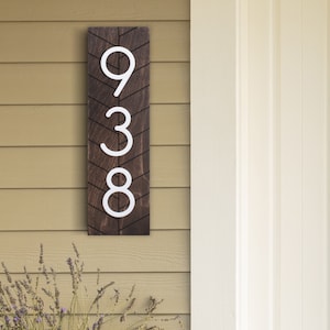 May include: A wooden house number sign with a chevron pattern. The numbers 938 are painted in white on the brown sign.