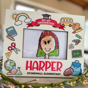 May include: A white wooden picture frame with a colourful graduation theme. The frame has a drawing of a child inside and the text "2024 My 1st Graduation" and "Harper Stonewall Elementary".