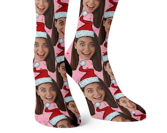 May include: A pair of pink socks with a repeating pattern of a woman's face wearing a Santa hat. The socks are pink with white accents and a festive design.