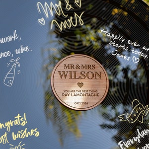 May include: A black vinyl record with gold lettering that says "Mr & Mrs" and "Happily ever after starts today. James." A wooden circle with the text "MR & MRS WILSON" and "YOU ARE THE BEST THING RAY LAMONTAGNE 09.12.2024" is placed on the record.