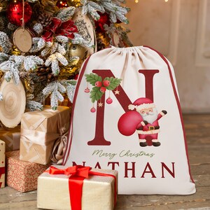 May include: A white canvas drawstring bag with a red letter N, a cartoon Santa Claus holding a red bag, and the text "Merry Christmas Nathan".