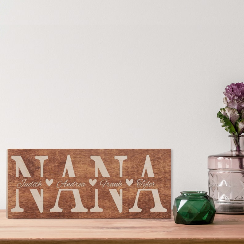 May include: Wooden sign with the word "NANA" spelled out in large letters. Below the word "NANA" are the names "Judith", "Andrea", "Frank", and "Tyler" with a heart symbol between each name.