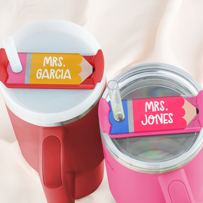 May include: Two red and pink stainless steel tumblers with lids and straws. The lids have pencil-shaped name tags that say "MRS. GARCIA" and "MRS. JONES".