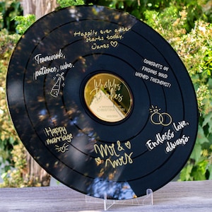May include: A black vinyl record with gold lettering. The record has a gold mirror center with the words "Mr & Mrs" and "Happily ever after starts today." The record also has the words "Teamwork, patience, wine." and "Happy marriage." on it.