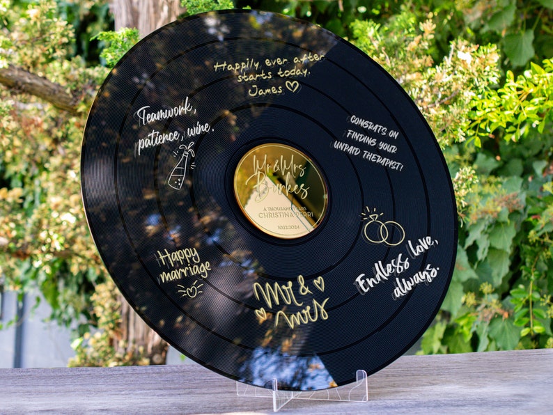 May include: A black vinyl record with gold lettering. The record has a gold mirror center with the words "Mr & Mrs" and "Happily ever after starts today." The record also has the words "Teamwork, patience, wine." and "Happy marriage." on it.