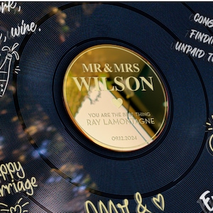 May include: A gold-colored vinyl record with a gold mirror disc that says "MR & MRS WILSON" with a heart and the text "YOU ARE THE BEST THING RAY LAMONTAGNE 09.12.2024". The record has black and white handwritten text around the edge, including "Teamwork, Patience, Wine", "Happy Marriage", "Congrats on finding your unpaid therapist", and "Endless Love".