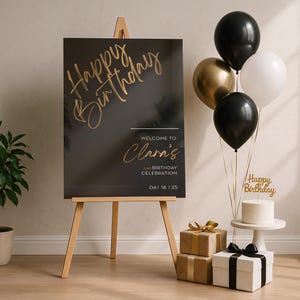 以下が含まれることがあります： 「Happy Birthday」と「Welcome to Clara's」のゴールドの文字が入った黒い看板がある誕生日のシーン。風船、プレゼント、そして「Happy Birthday」のケーキトッパーが付いたケーキが、お祝いの装飾を完成させています。