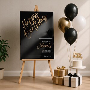 以下が含まれることがあります： 木製のイーゼルに飾られた黒と金の誕生日サイン。 「Happy Birthday」と「Clara's Birthday Celebrationへようこそ」の文字。 風船、ギフト、ケーキが華やかなシーンを演出しています。