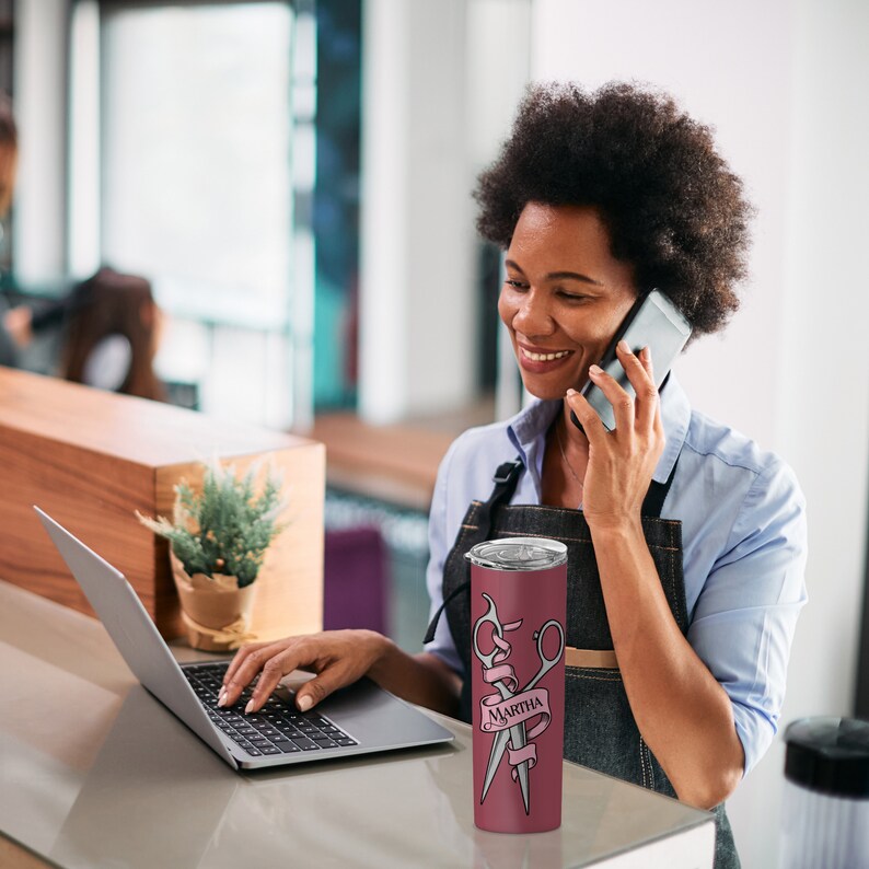 May include: A maroon stainless steel tumbler with a pink ribbon and two silver scissors with the name "Martha" on the ribbon.