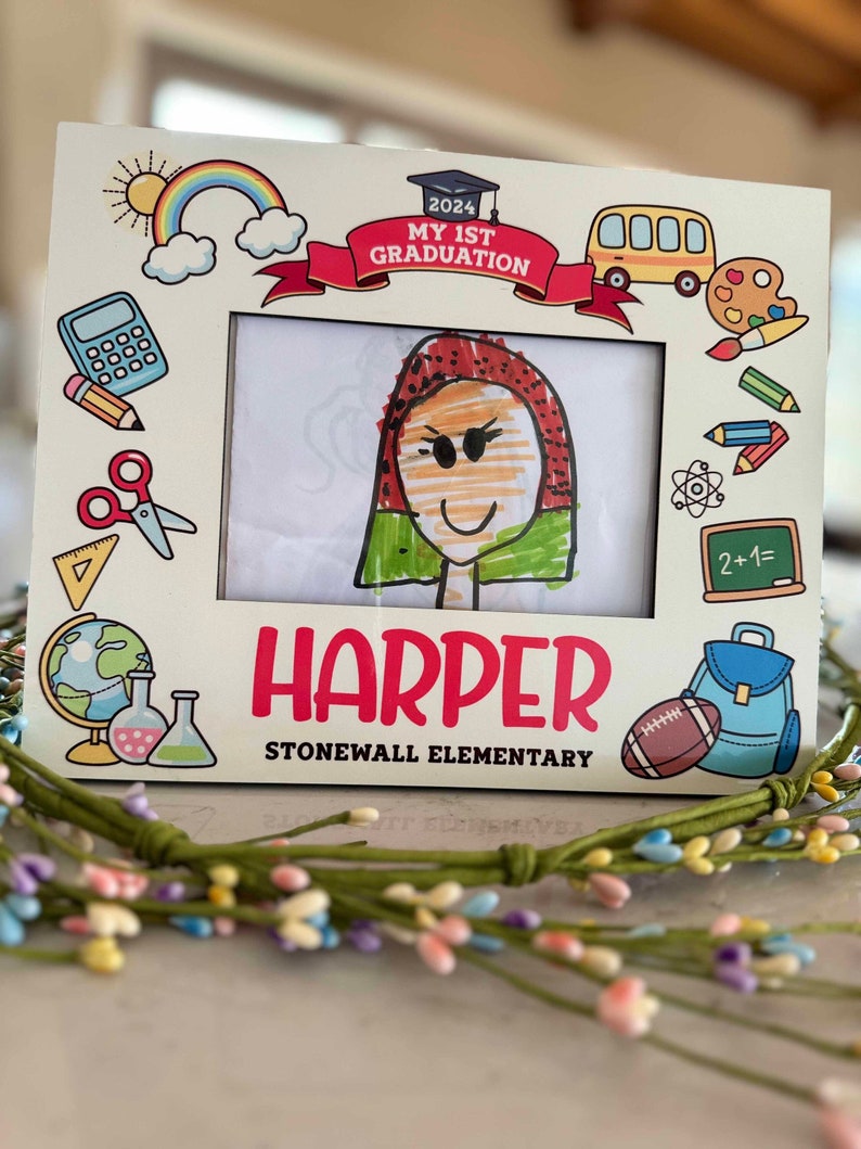 May include: A white wooden picture frame with a colourful graduation theme. The frame has a drawing of a child inside and the text "2024 My 1st Graduation" and "Harper Stonewall Elementary".