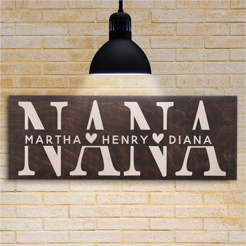 May include: A brown wooden sign with the word "NANA" in white letters. The names "MARTHA", "HENRY", and "DIANA" are written below the word "NANA" with hearts between each name.