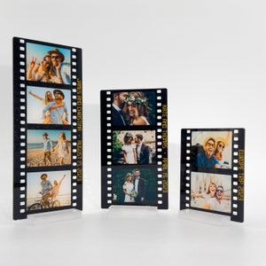 May include: Three black film strip photo displays with clear acrylic bases. Each strip features multiple photos. Text on the displays reads: "JAMES AND CHRISTINA - AUGUST 17, 2023", "KATE AND THOMAS - APRIL 19, 2023", and "EUROPE TRIP 2023".