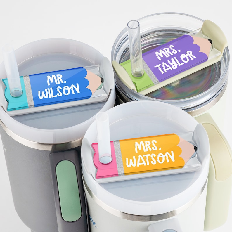 May include: Three stainless steel travel mugs with lids and straws. Each mug has a colorful pencil-shaped tag with a teacher's name on it. The tags read "Mr. Wilson", "Mrs. Taylor", and "Mrs. Watson".