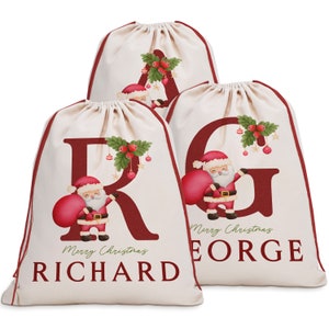 May include: Three personalized Christmas gift bags with red and white Santa Claus designs. The bags are made of natural canvas fabric and feature the letters R, G, and A with the names Richard, George, and the text "Merry Christmas".