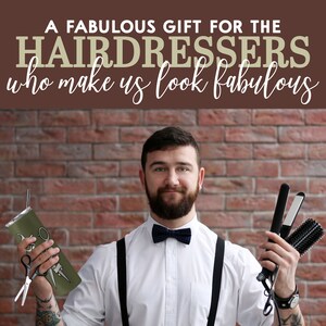 May include: A man wearing a white shirt, black bow tie, and suspenders holds a green tumbler with a pair of scissors and a black curling iron with a brush attachment. The background is a brick wall with the text "A FABULOUS GIFT FOR THE HAIRDRESSERS who make us look fabulous".