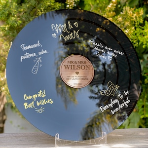 May include: A black vinyl record with a gold inscription that reads "Happily ever after starts today. James." and "Everyday to be wonderful." The record also has a gold inscription that reads "Teamwork, patience, wine." and "Congrats! Best wishes." A wooden plaque with the text "MR & MRS WILSON" is attached to the record. The plaque also has the text "YOU ARE THE BEST THING RAY LAMONTAGNE 0912.3004".