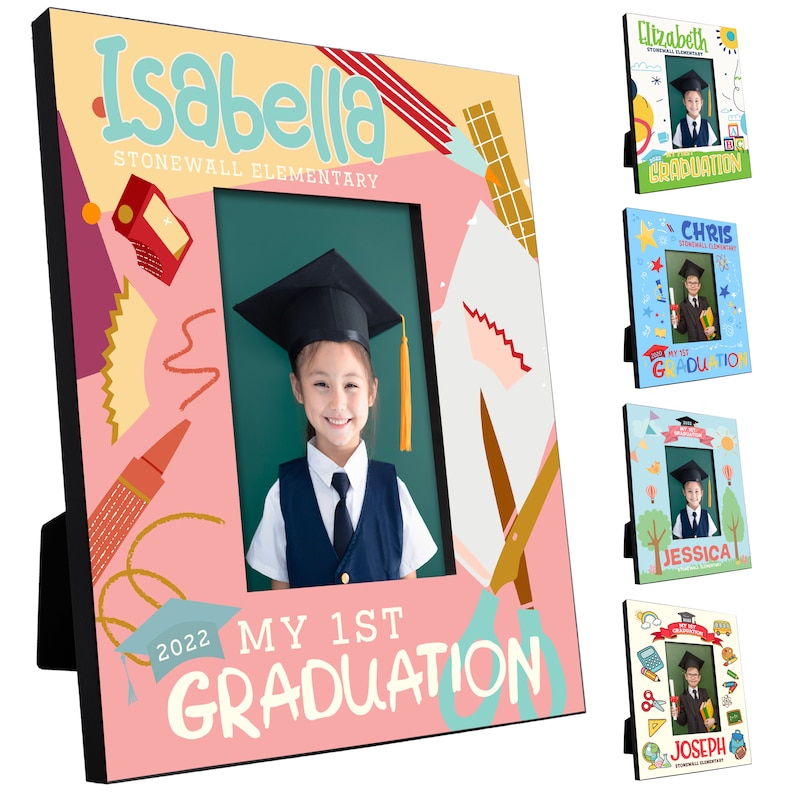 May include: A pink and yellow graduation photo frame with a colourful design featuring a graduation cap, scissors, and pencils. The frame has a black border and a cutout for a 4x6 inch photo. The text "My 1st Graduation" is printed on the frame.